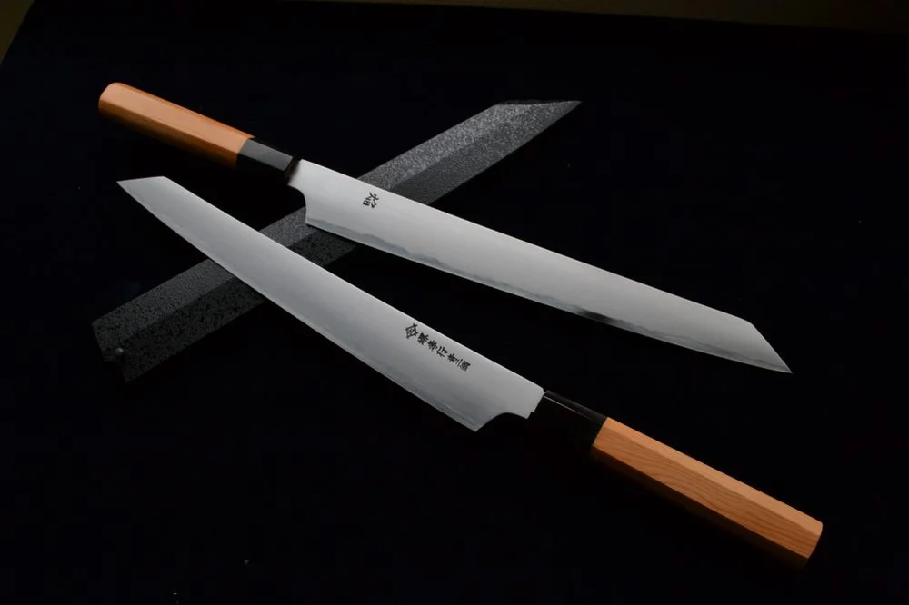 Two Sakai Takayuki yanagiba knives with orange handles on a black background
